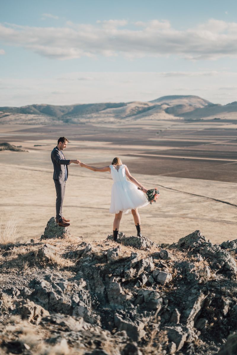A couple poses together on dramatic volcanic rocks with mountains and desert landscape in the background.