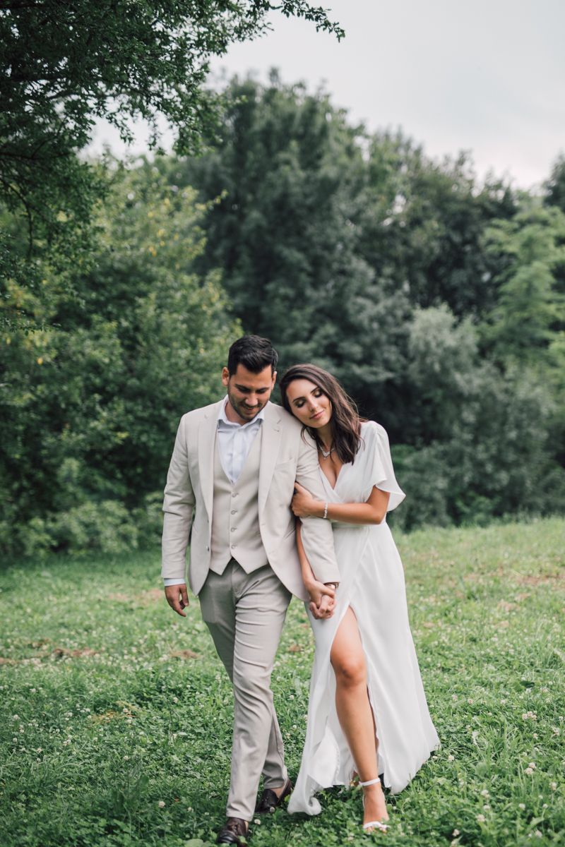 A couple in wedding attire walks together through a lush green meadow on their special day.