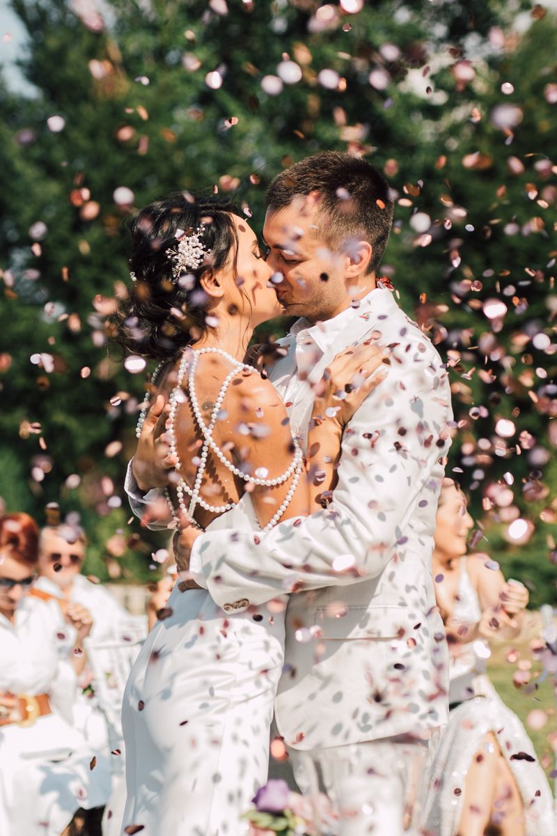 Romantic wedding moment with confetti flying through the air as couple embraces during outdoor celebration.