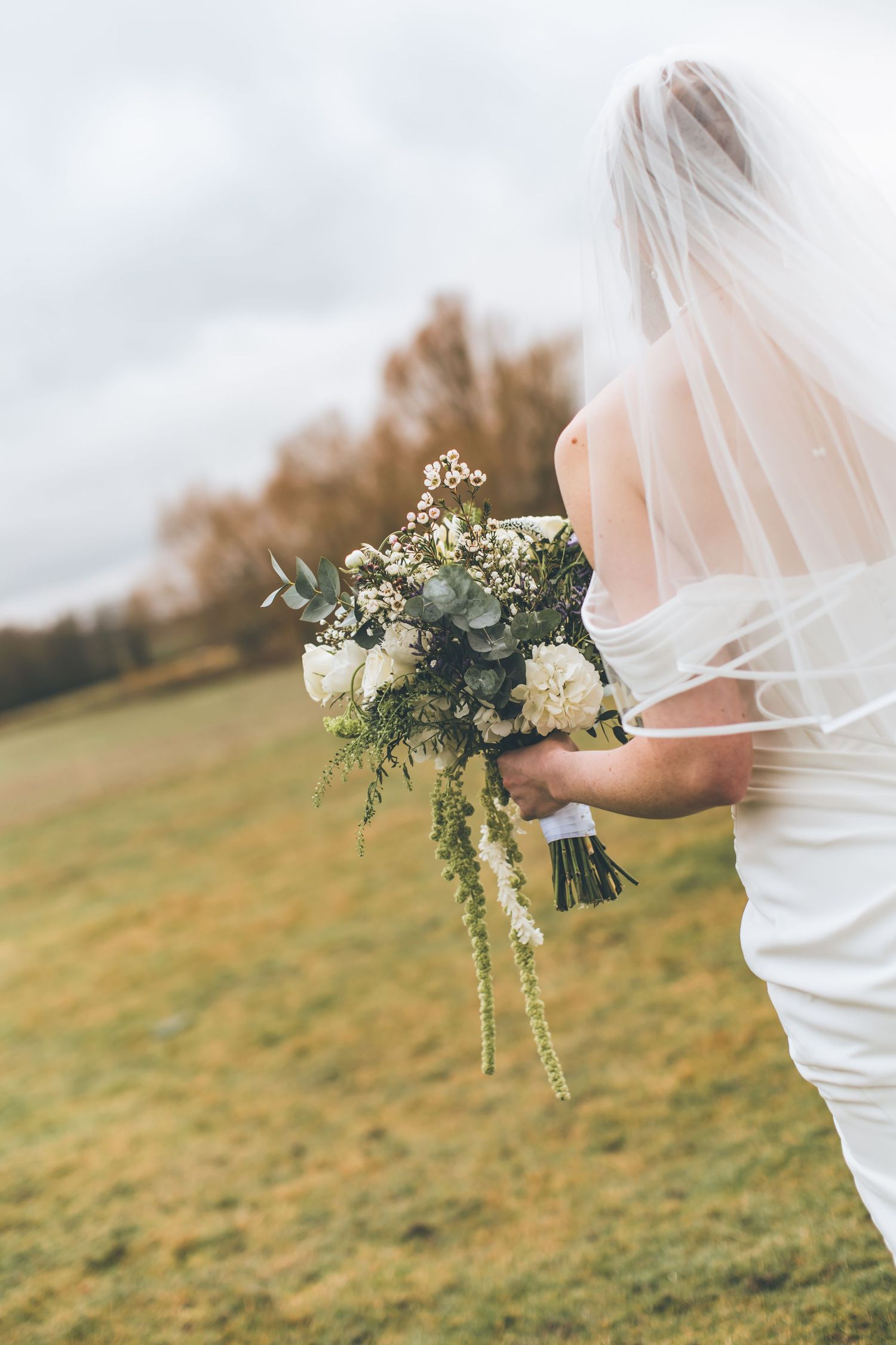 An elegant bridal bouquet featuring cream roses, delicate greenery and lace details against a wedding dress.