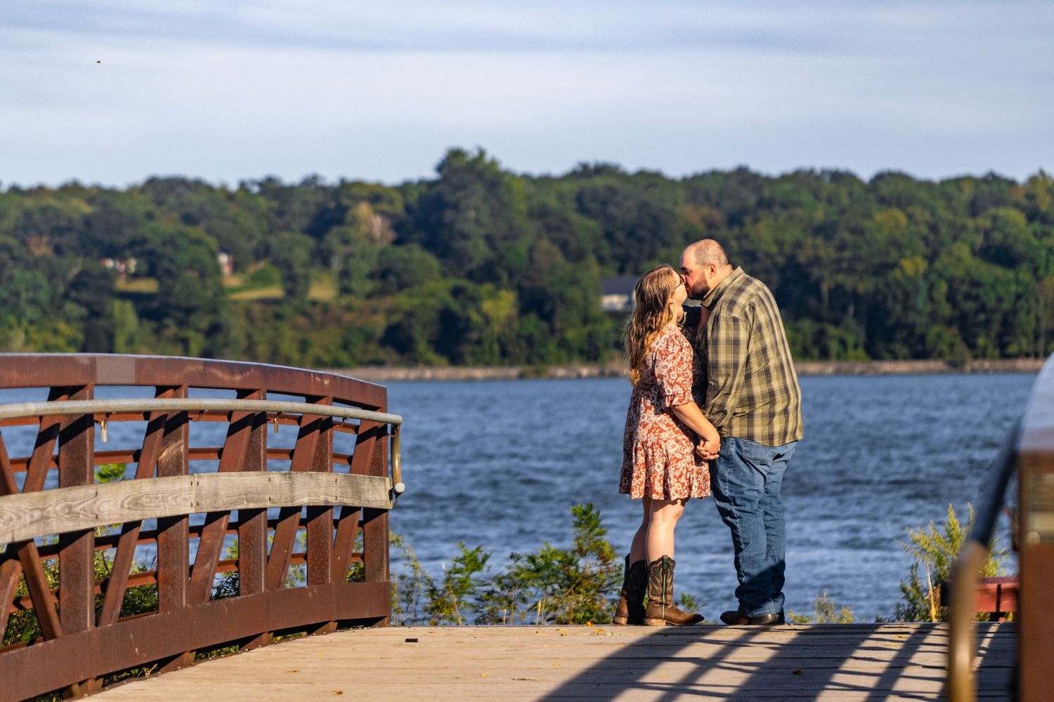Couple sharing an intimate moment on a wooden bridge over a lake at sunset.