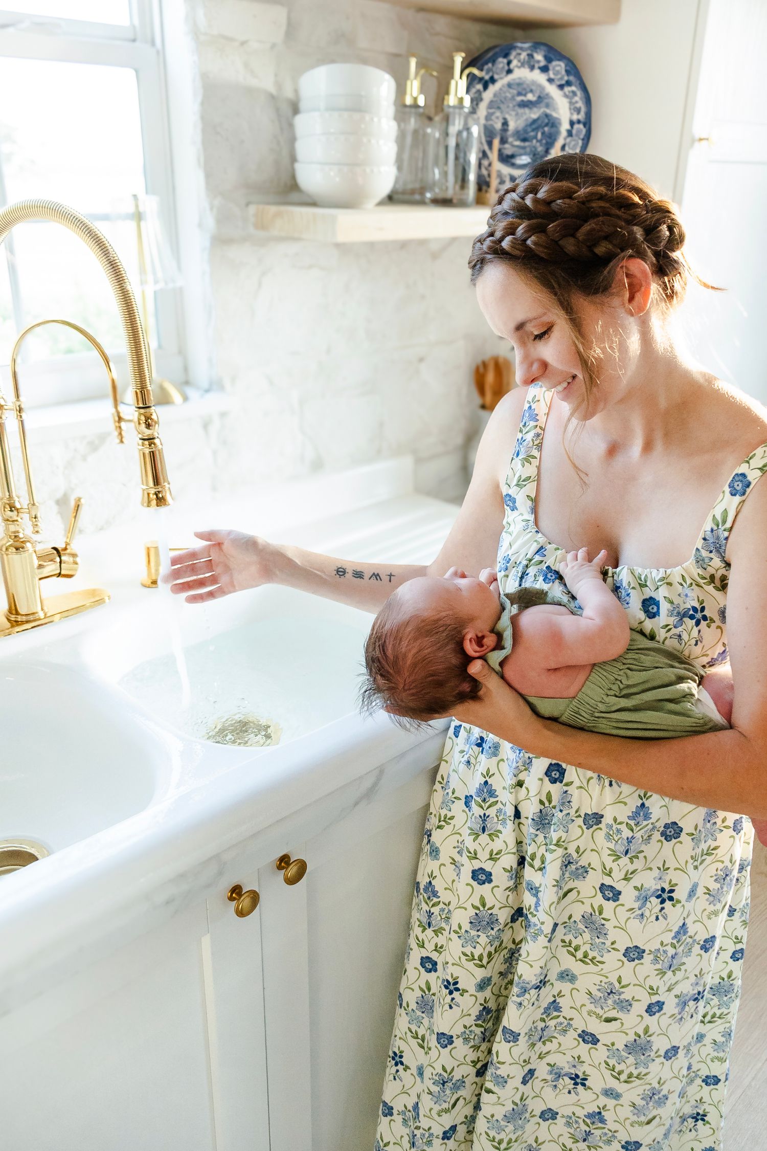 Mother looks tenderly at baby while she warms the water in the sink for her baby.