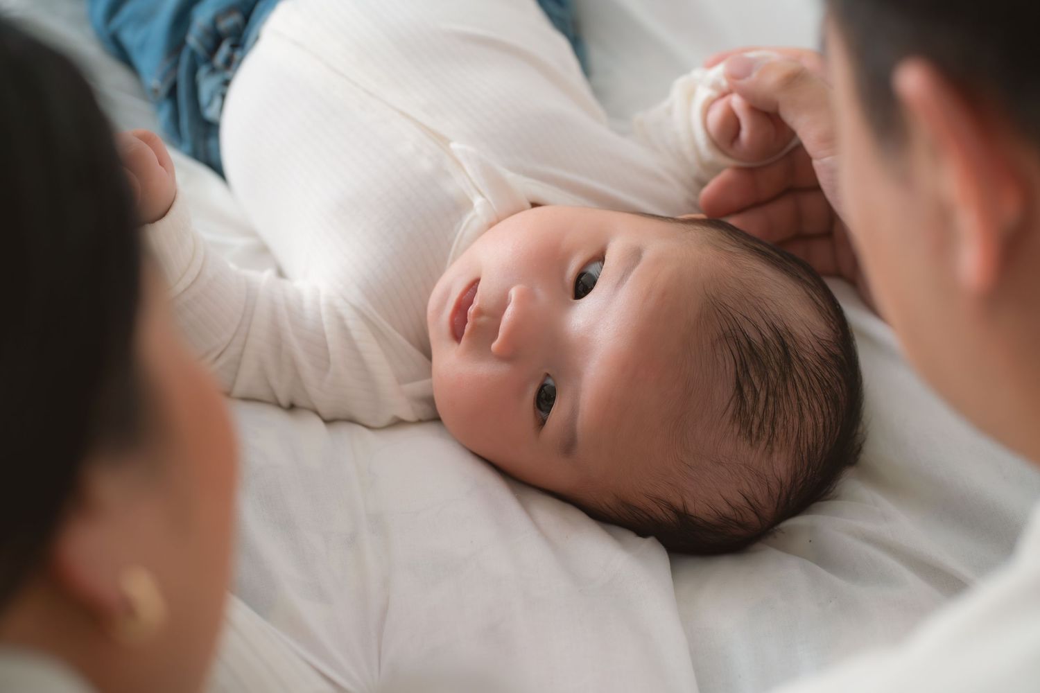 Baby in floral headband lying on white bedding with soft natural lighting.