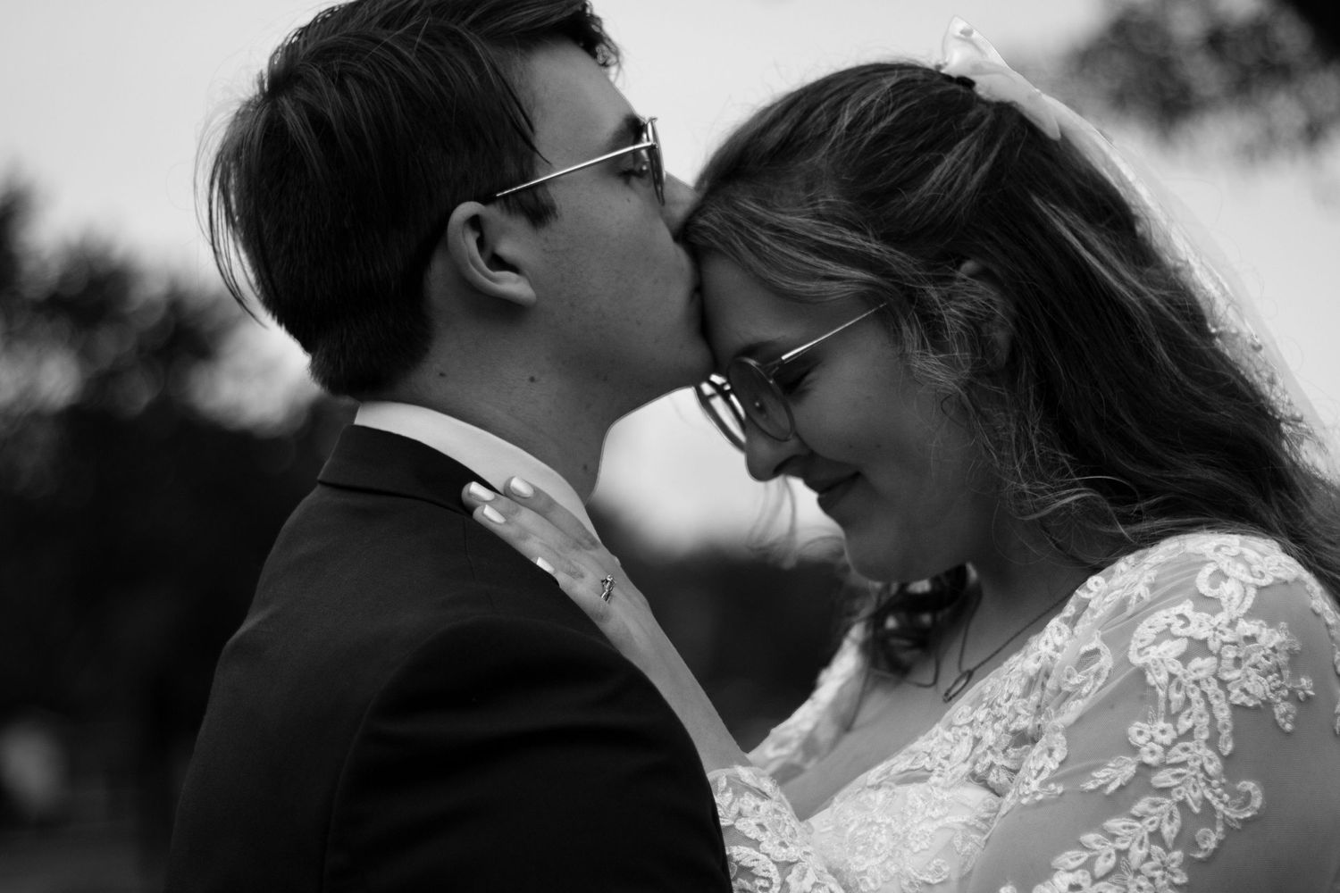 A black and white photograph capturing an intimate wedding moment outdoors.