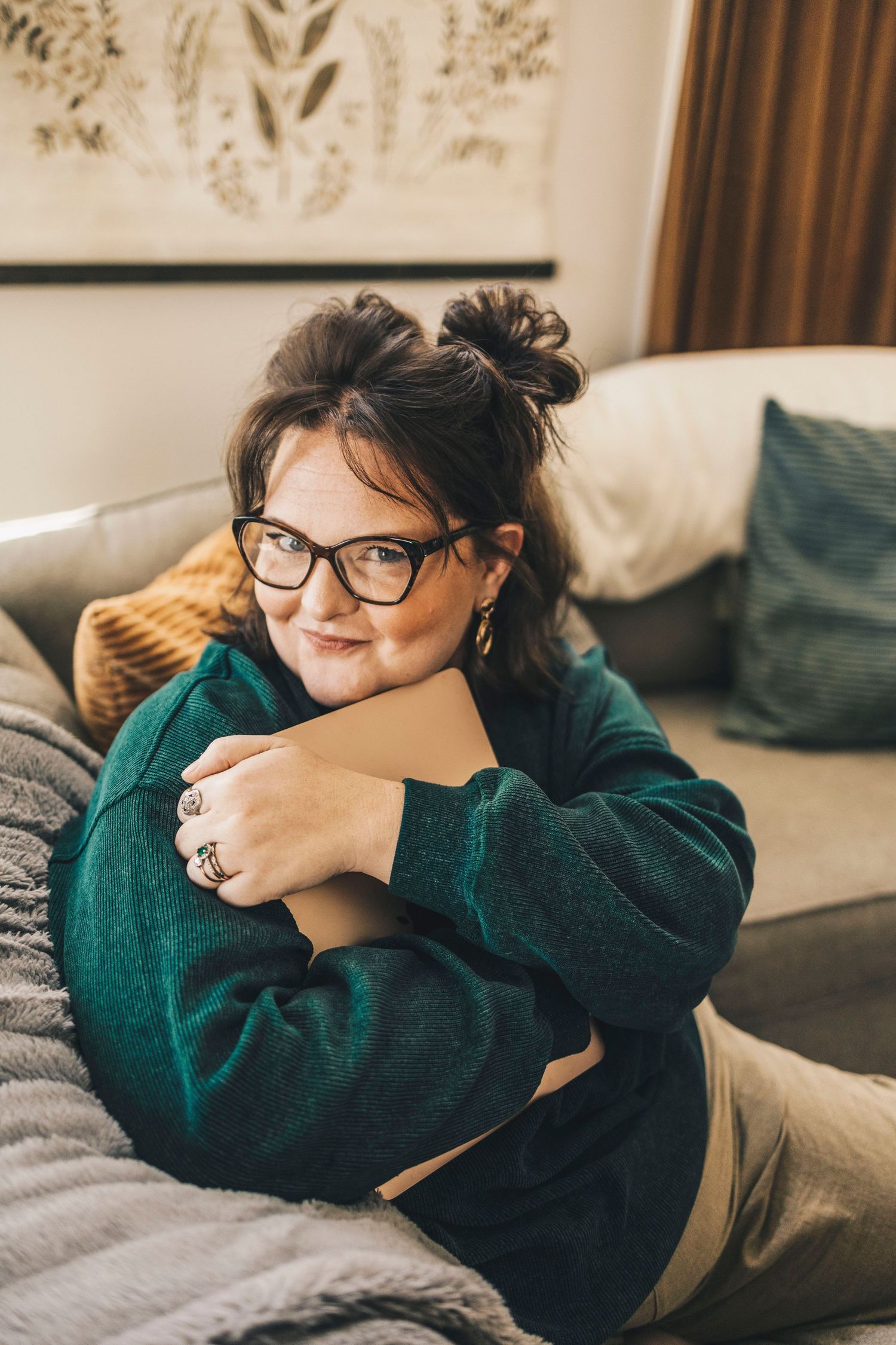 Woman in green sweater hugging notebook while lying on couch smiling warmly.