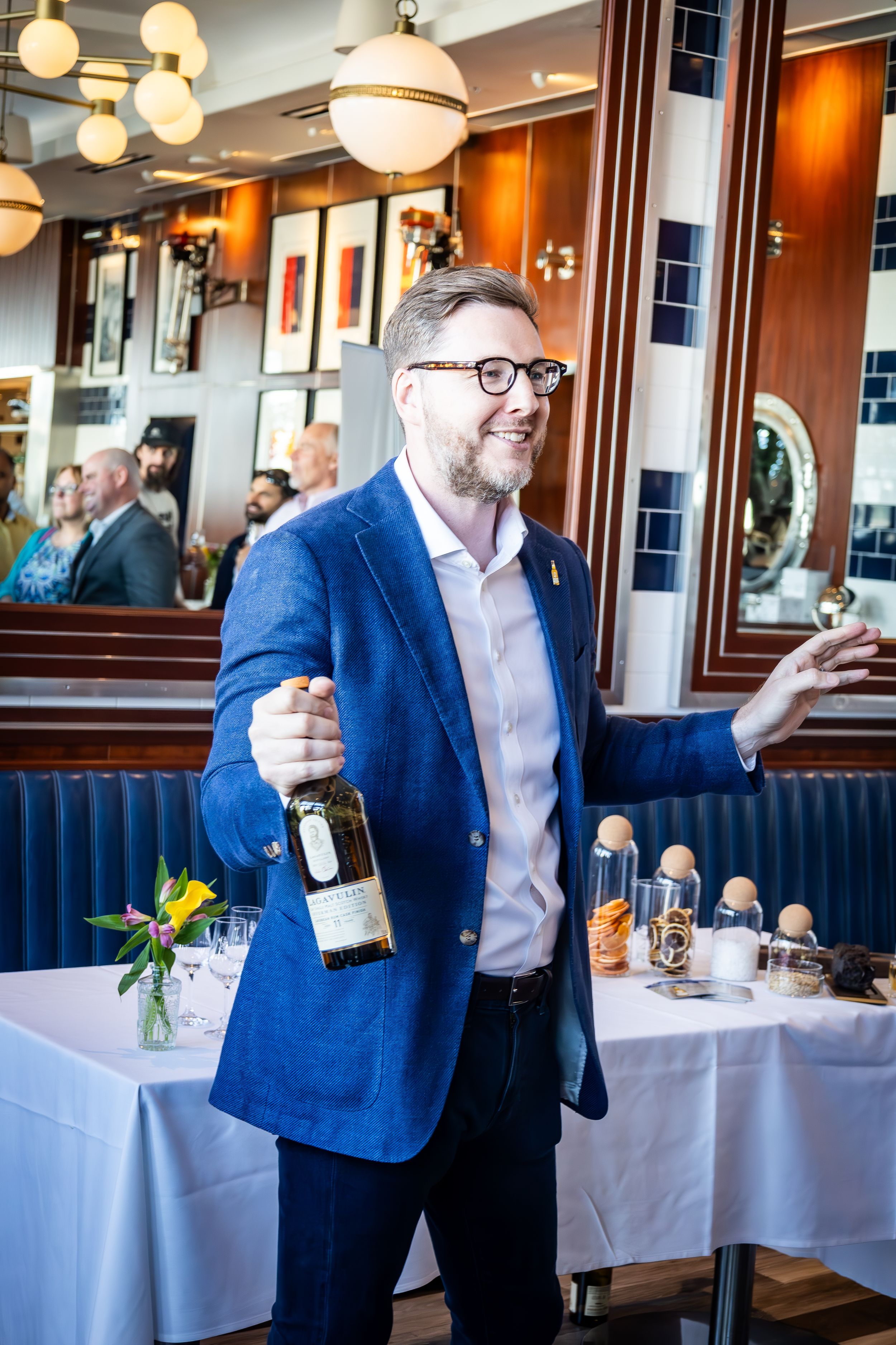 Restaurant patron in blue blazer and glasses holding wine bottle at upscale dining establishment.