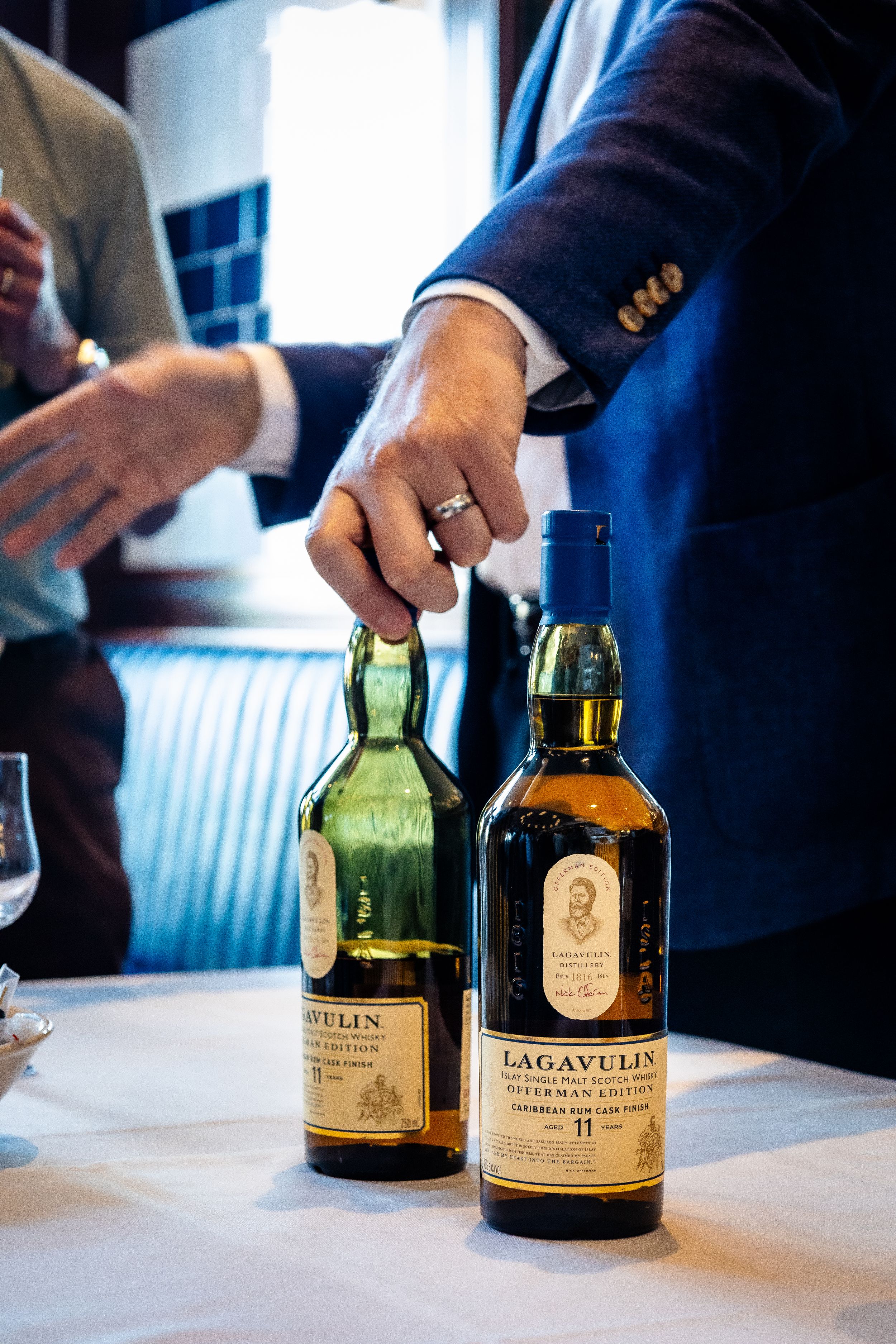 Close-up of Lagavulin whisky bottles on white tablecloth in restaurant setting.