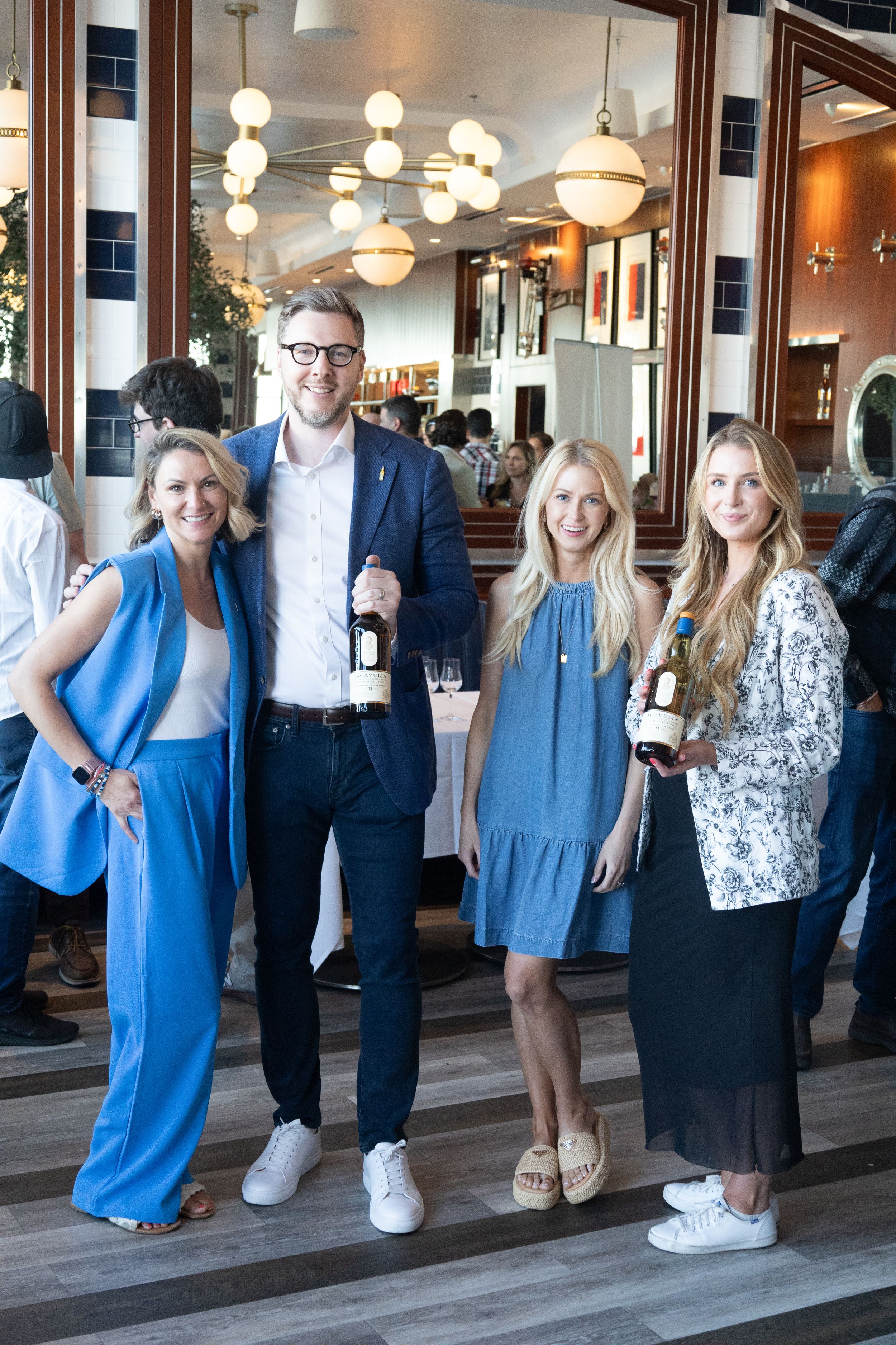 Group poses with wine bottles at upscale restaurant with modern lighting fixtures.