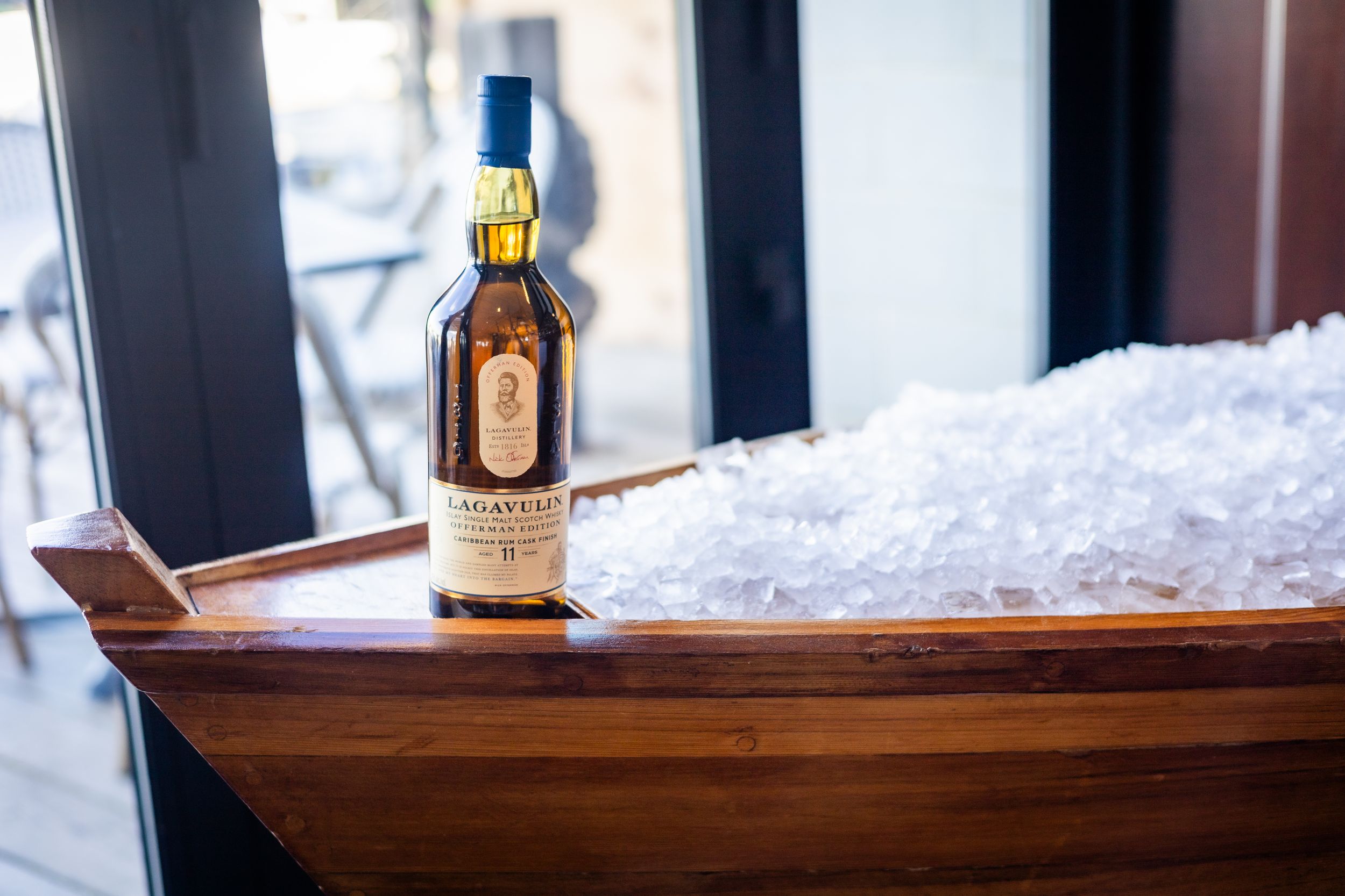 Bottle of Lagavulin whisky displayed on wooden surface with snow in background.