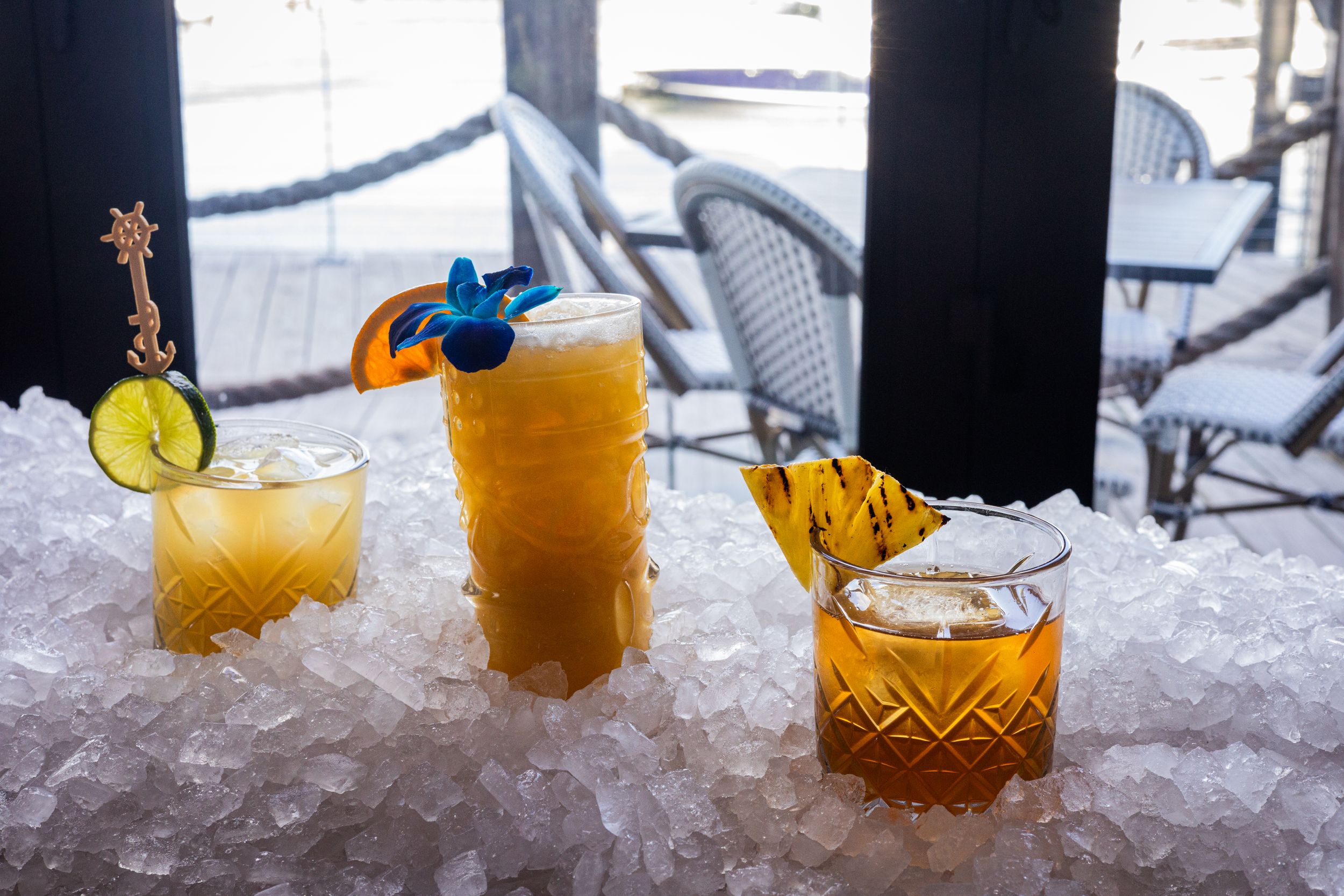 Three colorful craft cocktails served on crushed ice with garnishes and decorative glassware.