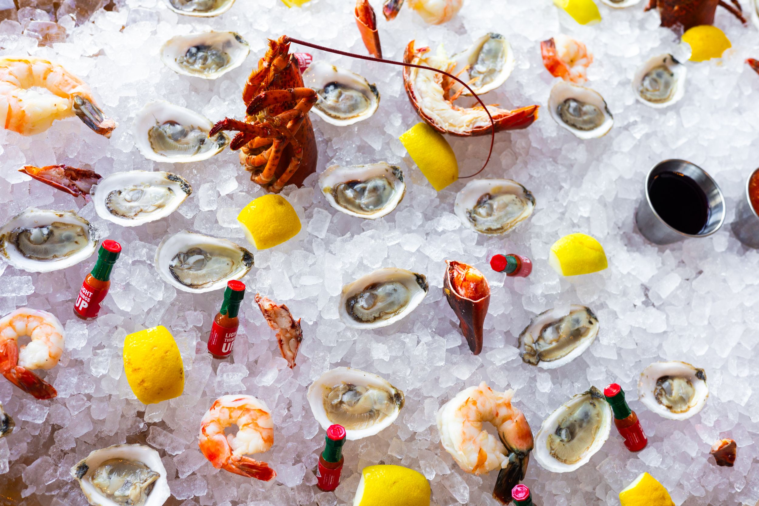 Fresh seafood display with oysters, shrimp, and crawfish arranged on ice with lemon wedges.
