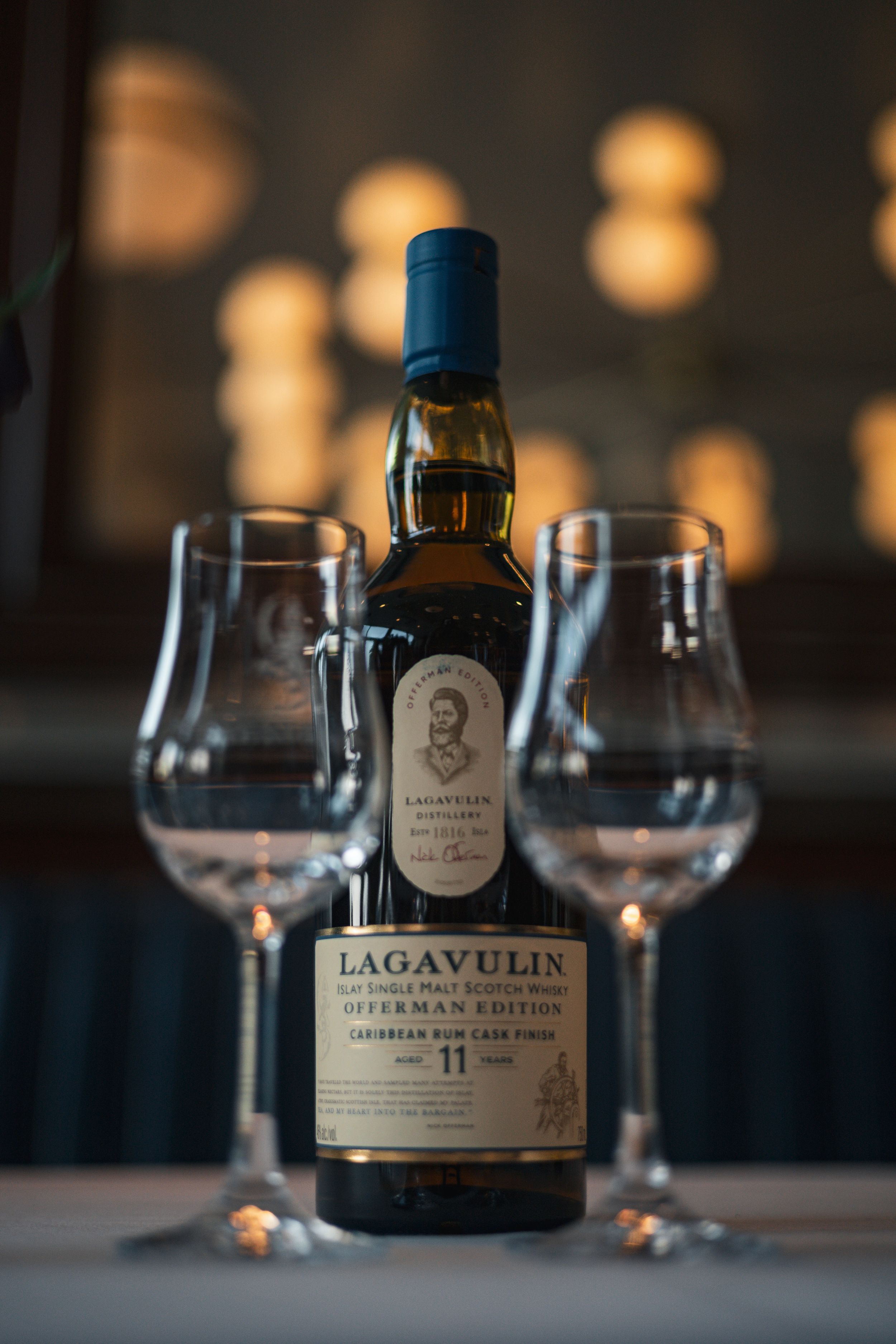 Bottle of Lagavulin whisky displayed with two empty glasses in moody lighting.