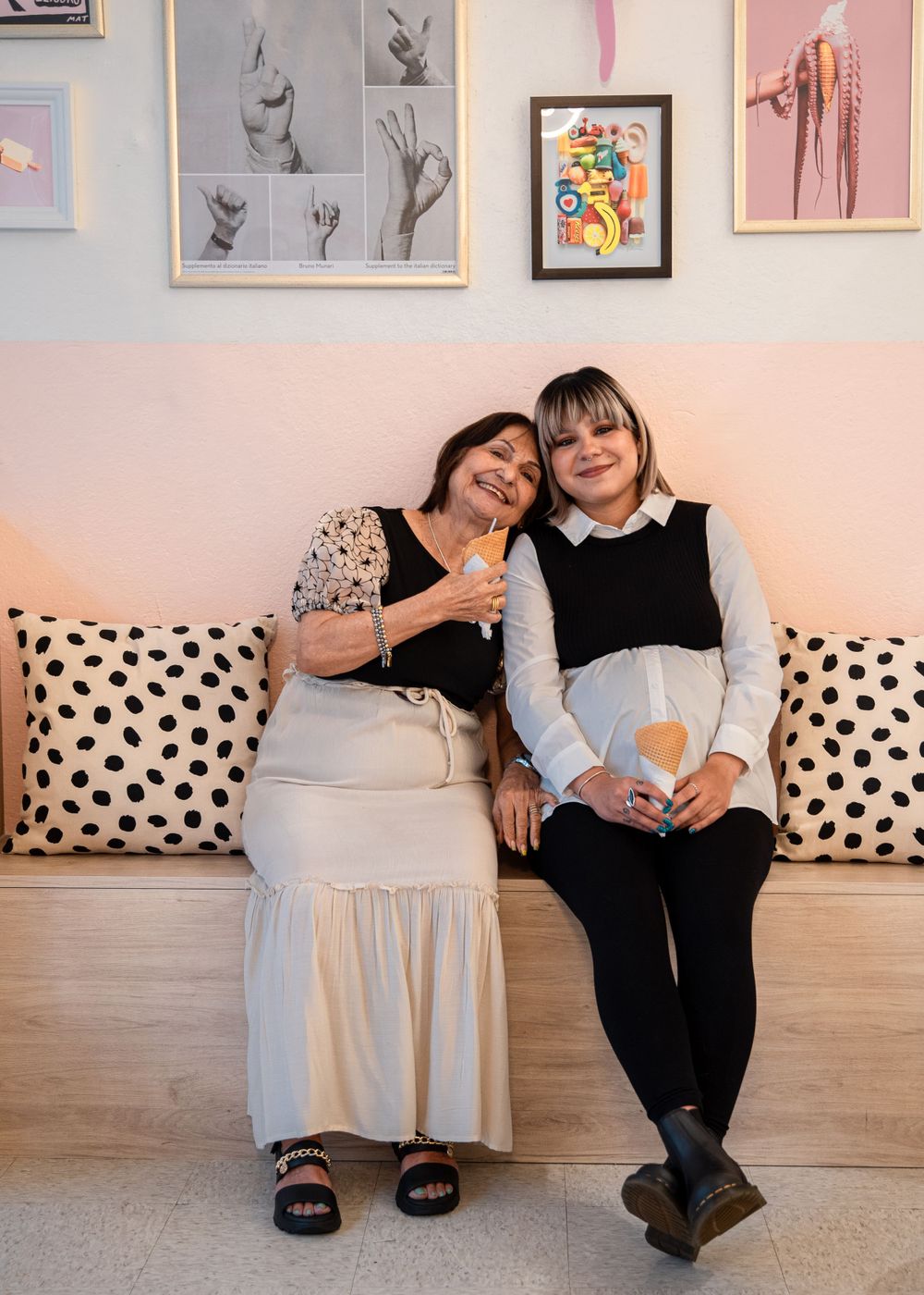 Two people relax on a polka dot couch beneath framed artwork on a pink wall.