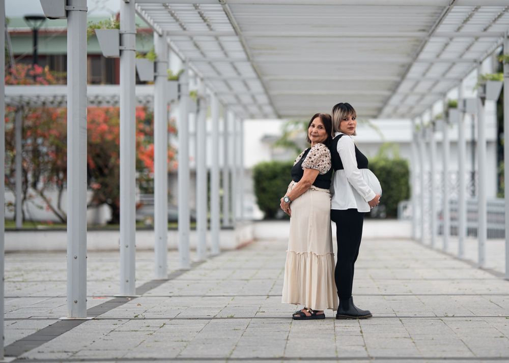 Two people pose together under a covered walkway with white pillars.