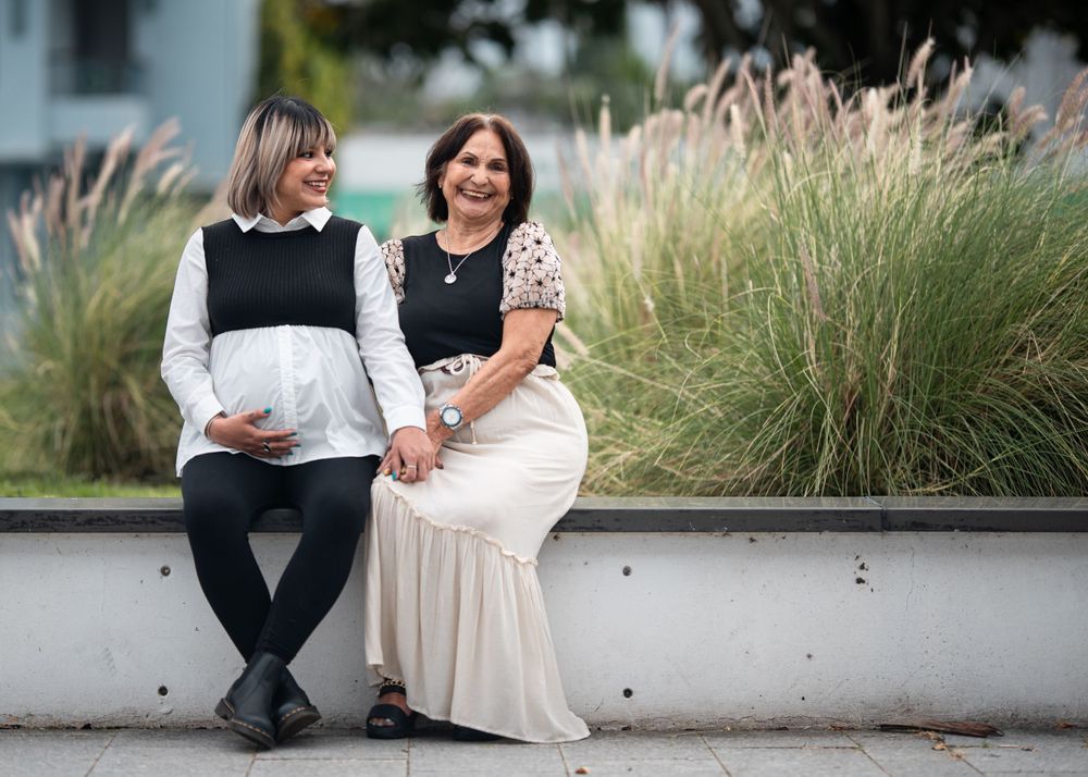 Two people sit together on a concrete ledge with ornamental grasses in the background.