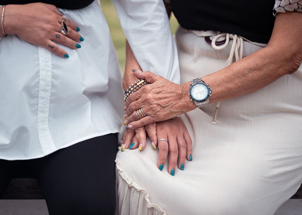 Close-up of hands with rings and blue nail polish resting together on white fabric.