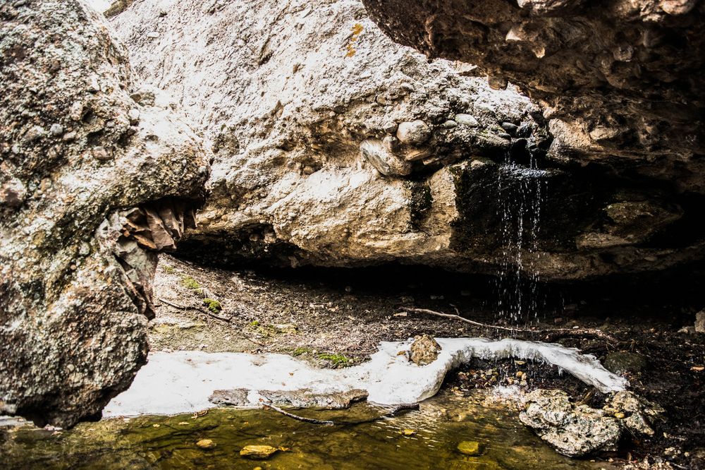 A small waterfall flows over rocky outcroppings with patches of snow in winter.