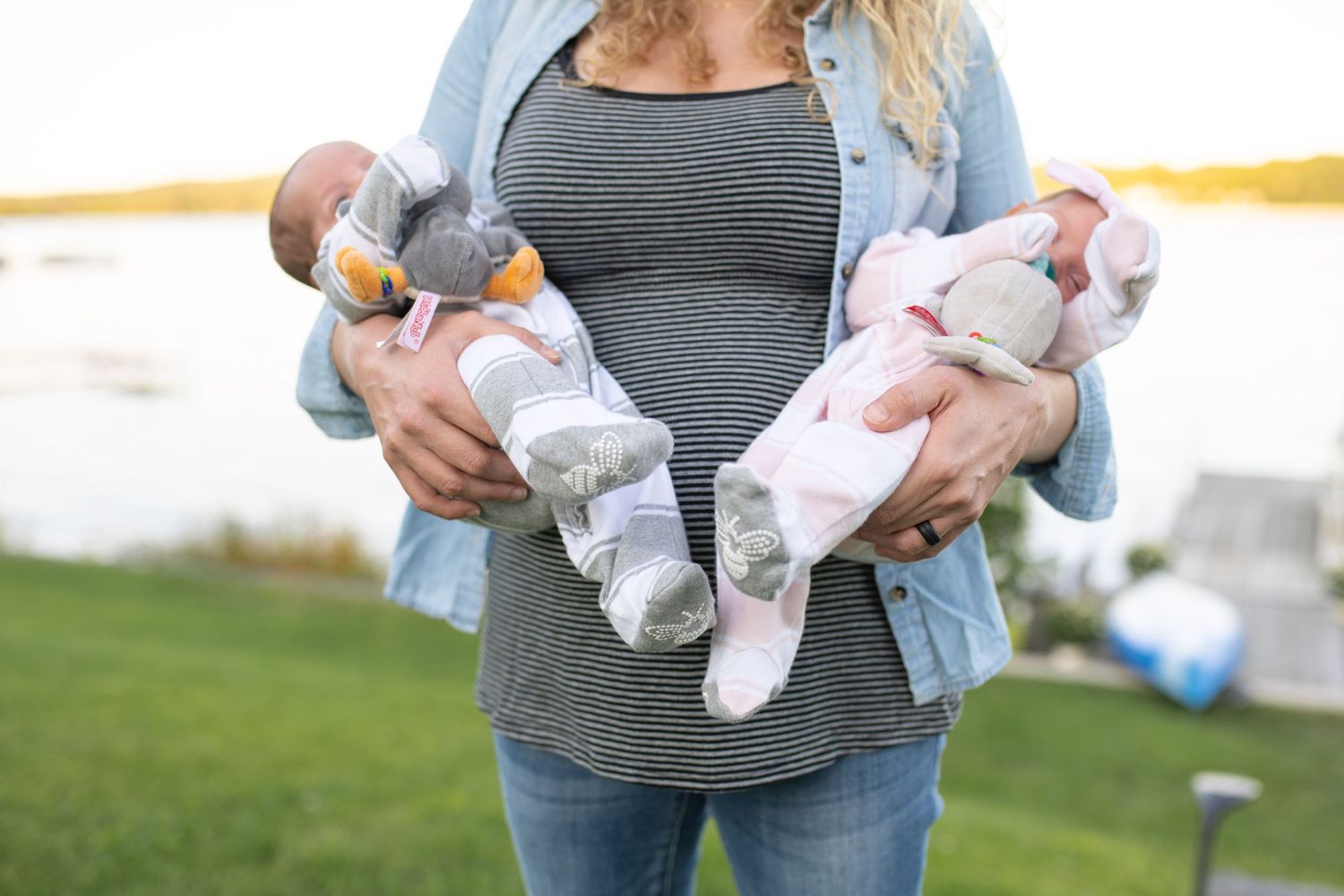 A person holds two infant onesies with baby socks and clothing items outdoors.