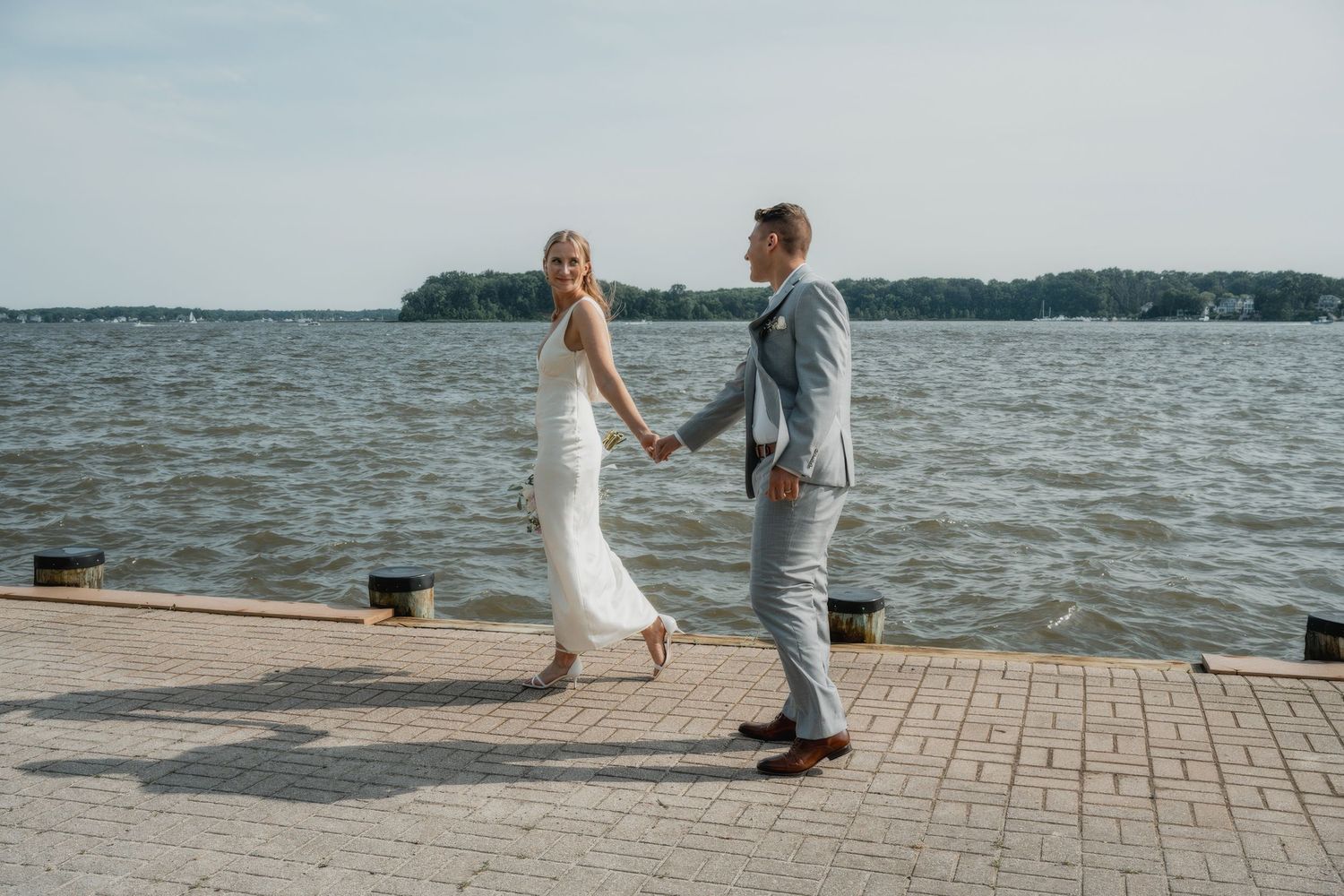 A couple shares a tender moment on a waterfront brick pathway.
