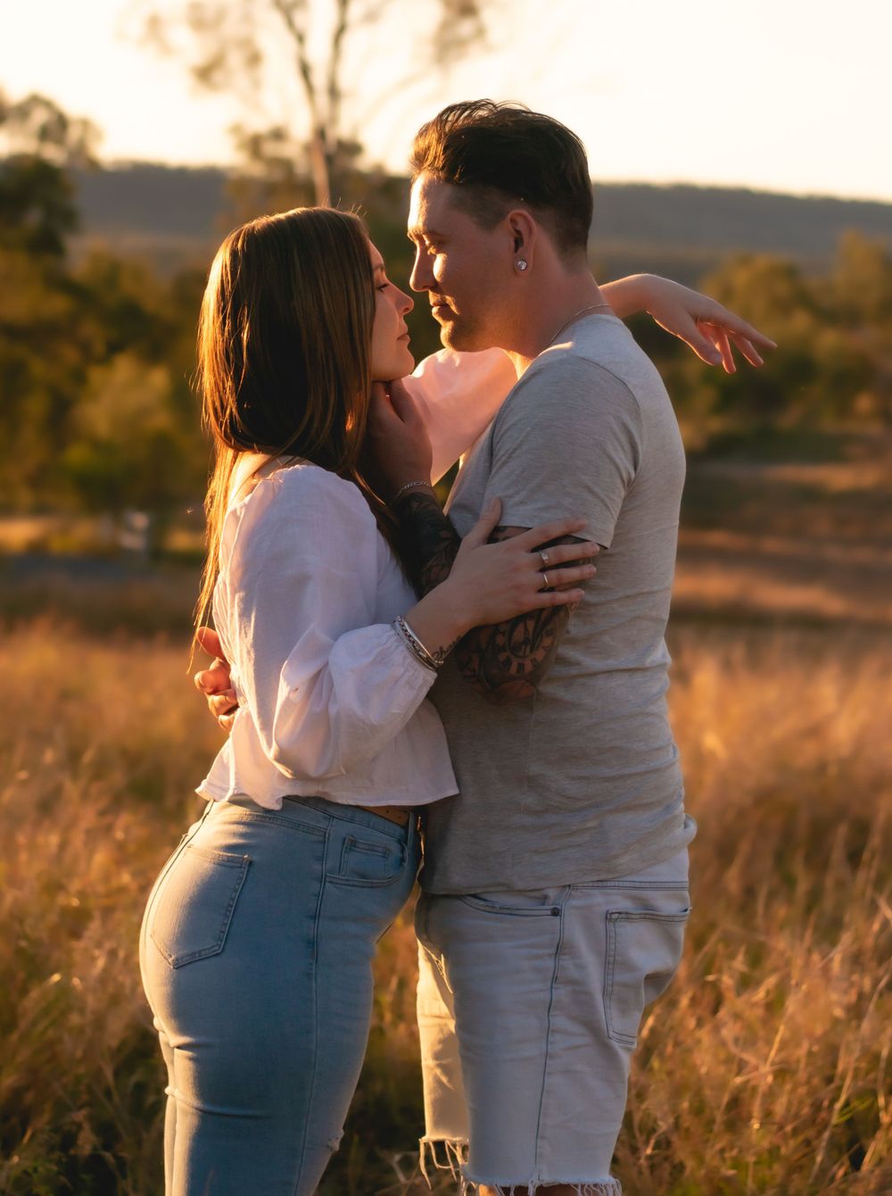 Romantic couple embracing in field during warm sunset light.
