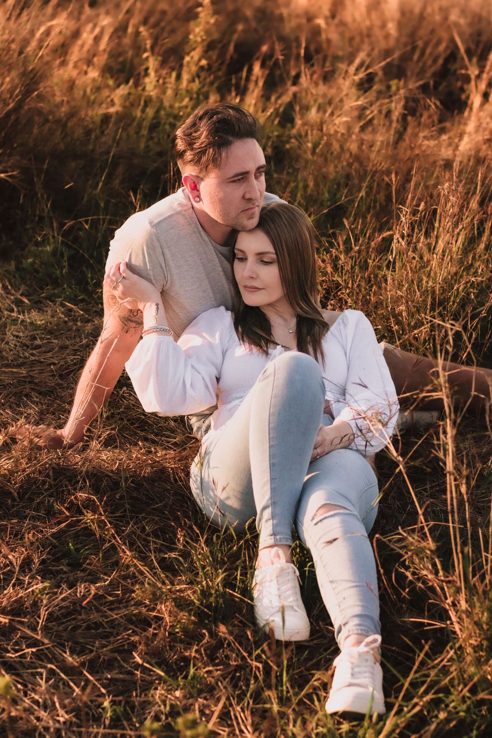 Couple relaxing together in field of tall grass during sunset.