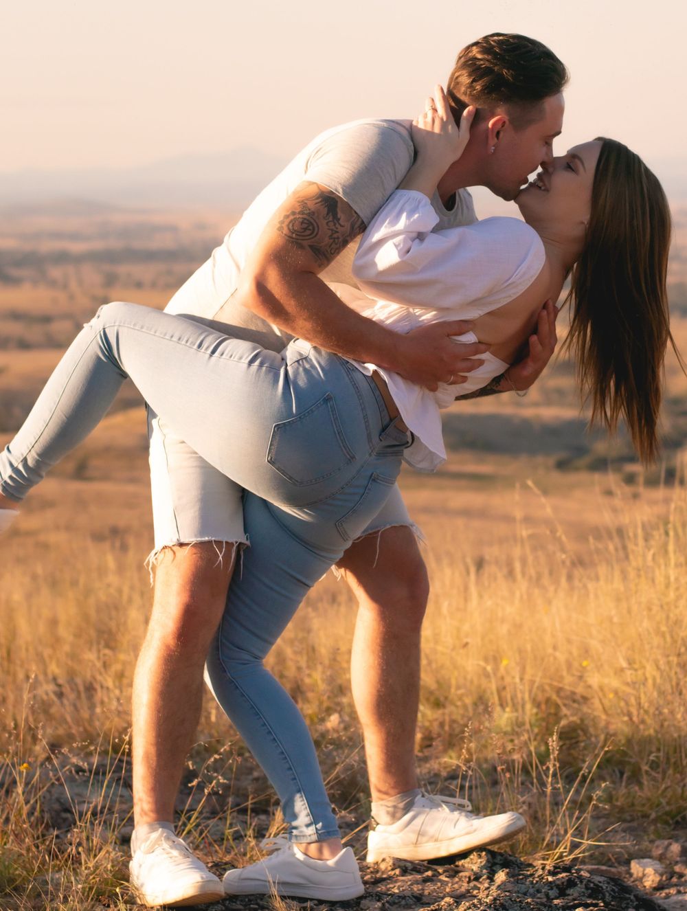 Playful couple sharing romantic dip pose in sunset field.