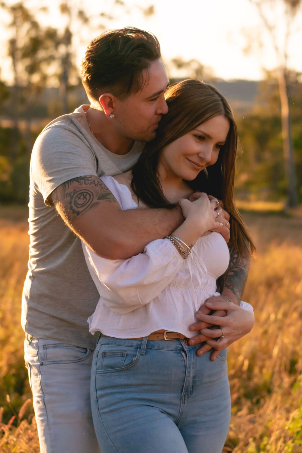 Intimate moment between couple in casual wear against sunset backdrop.