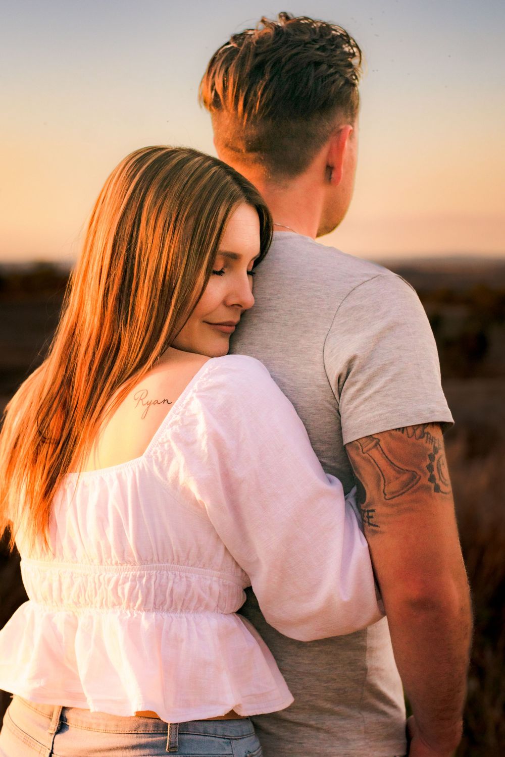 Couple in white and gray clothing embracing during sunset with warm lighting.