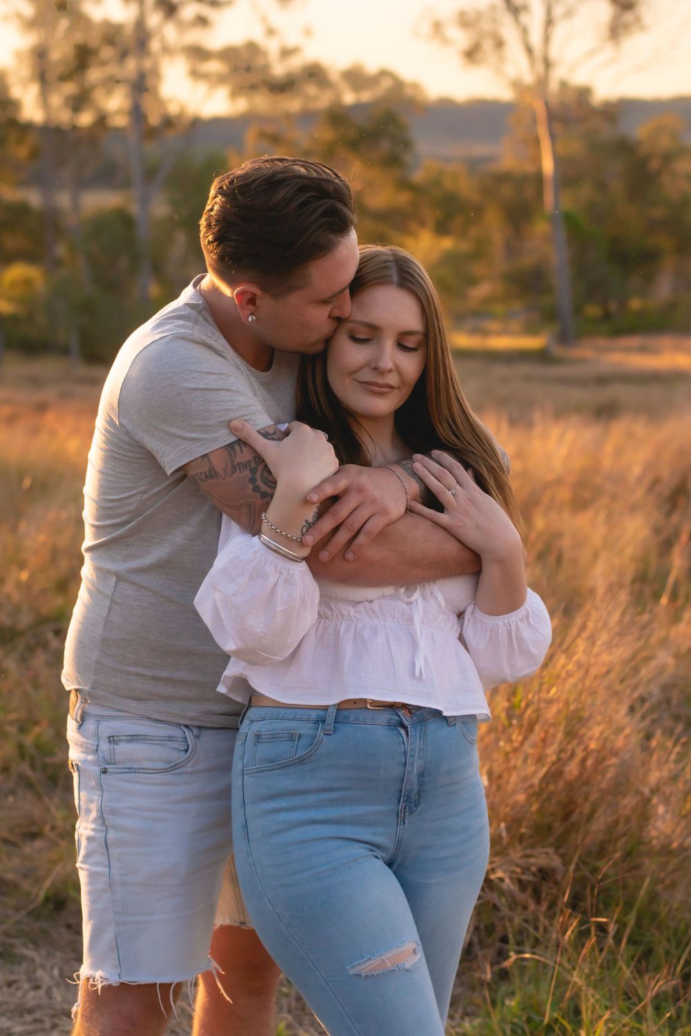 Tender embrace between couple in casual wear during golden hour in nature.