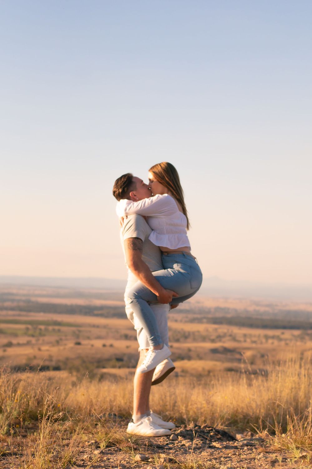 Affectionate couple embracing on hilltop against sunset sky.