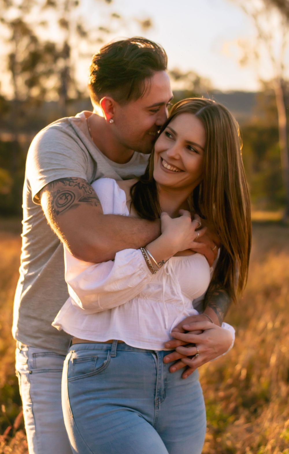 Couple sharing intimate embrace in golden sunset field.