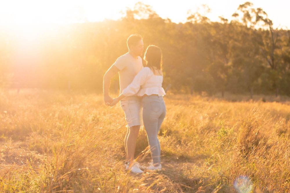 Silhouetted couple embracing in sunlit field during golden hour.