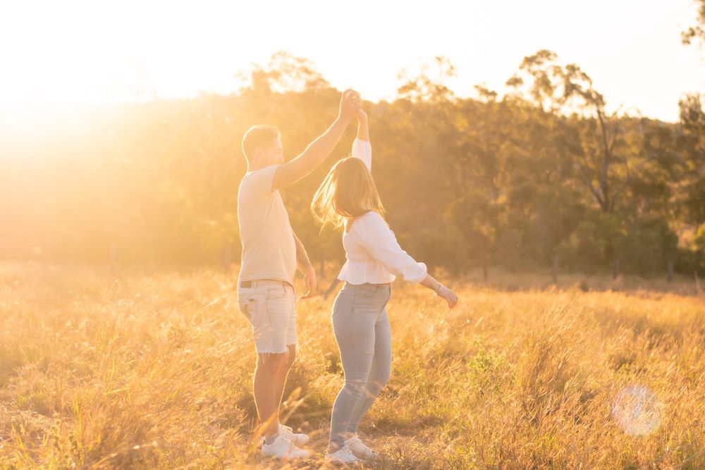Couple dancing joyfully in sunlit field at golden hour.