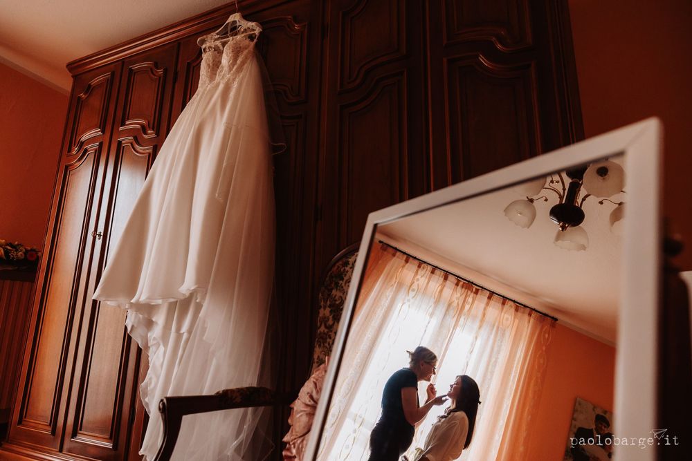 Wedding dress hanging on wooden wardrobe with reflection in mirror.