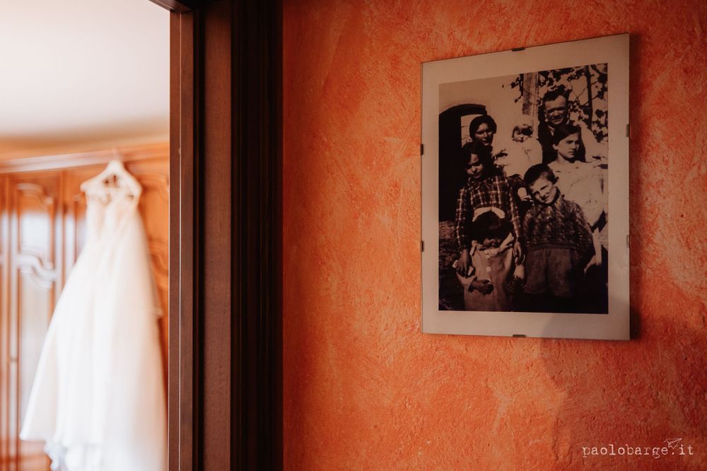 Wedding dress hanging in room with vintage framed artwork on orange wall.