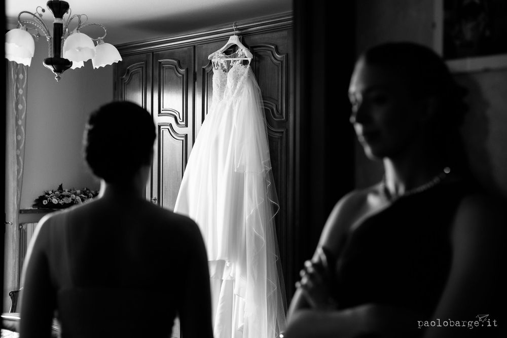 Silhouetted figures looking at an elegant wedding dress hanging in a dimly lit room.