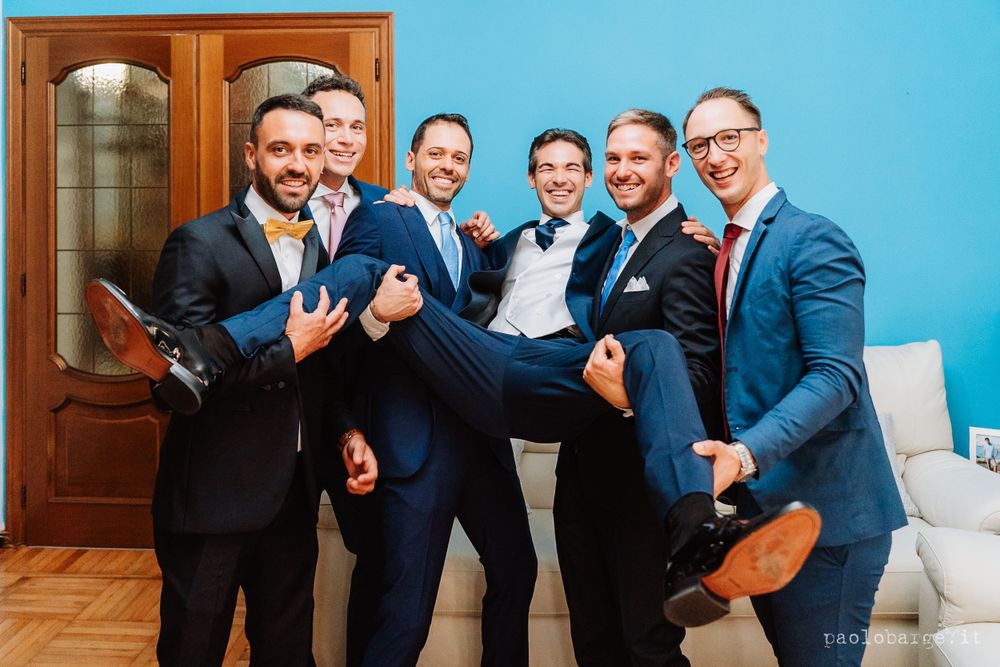 Groomsmen in navy suits playfully carrying the groom in a fun group photo.
