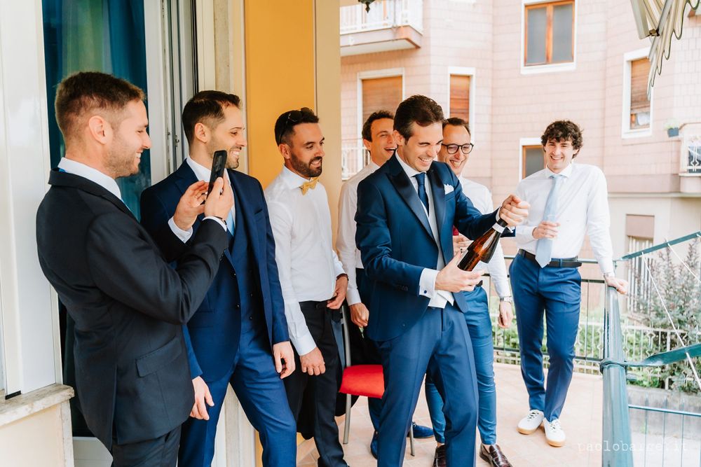 Group of friends in formal attire gathered on a balcony sharing drinks and laughter.