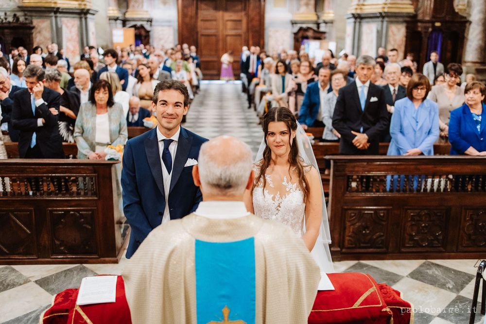 Couple standing at altar during traditional Catholic church ceremony with guests seated in wooden pews.