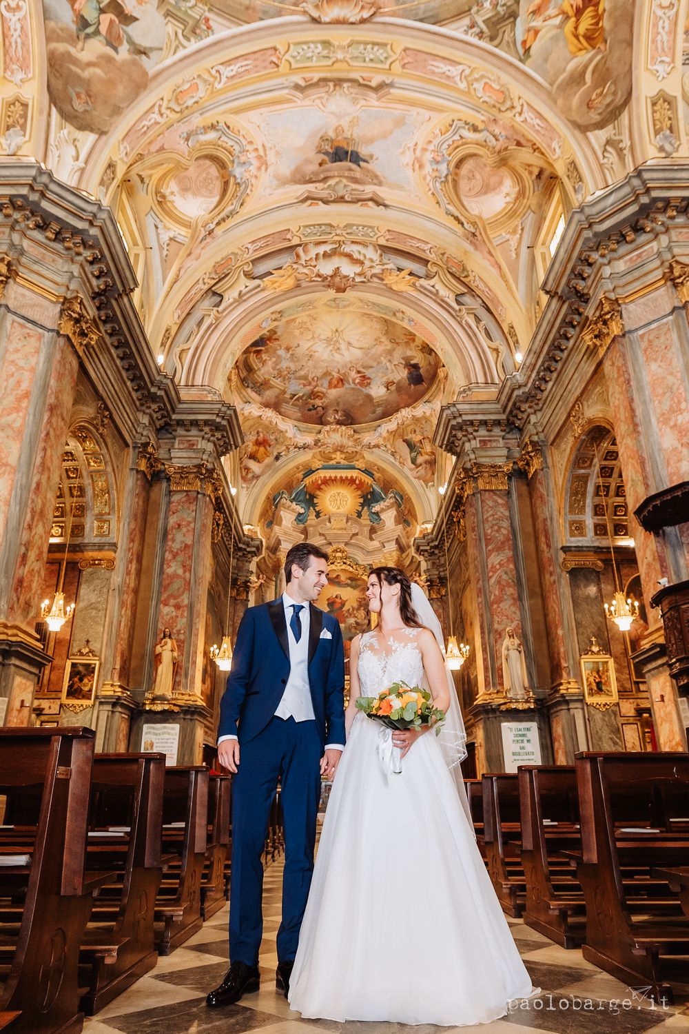 Wedding couple posing in ornate baroque church with stunning frescoed ceiling and gilded details.