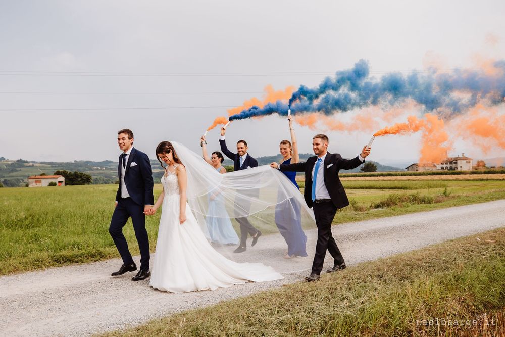 Wedding party walking on country road with colorful smoke bombs creating dramatic effect.