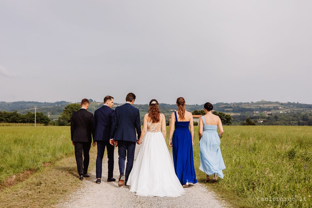 Wedding party walking together on rural path with rolling hills in background.