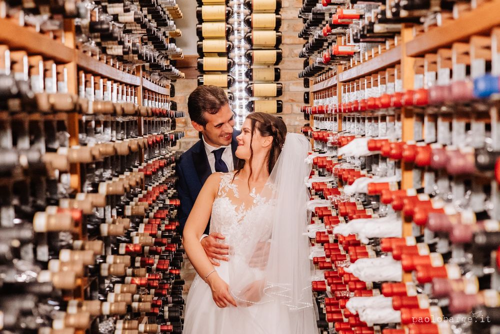 Wedding couple posing intimately in wine cellar surrounded by countless bottles.