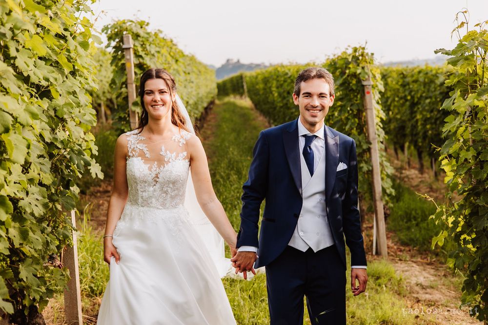 Joyful couple walking through vineyard rows in wedding attire.