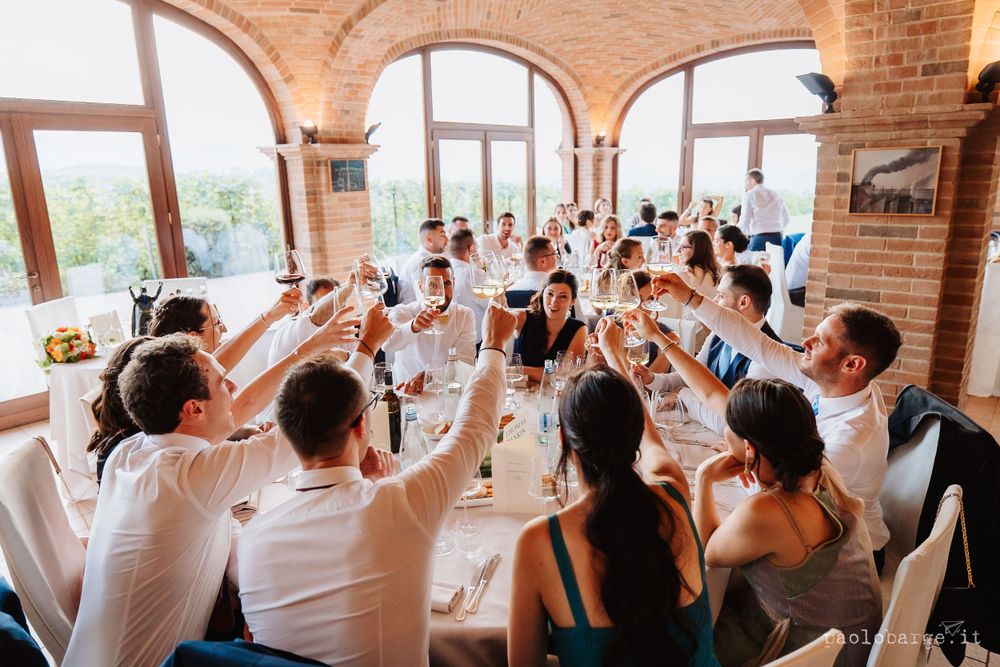 Wedding guests raise glasses in a toast during reception dinner under brick archways.