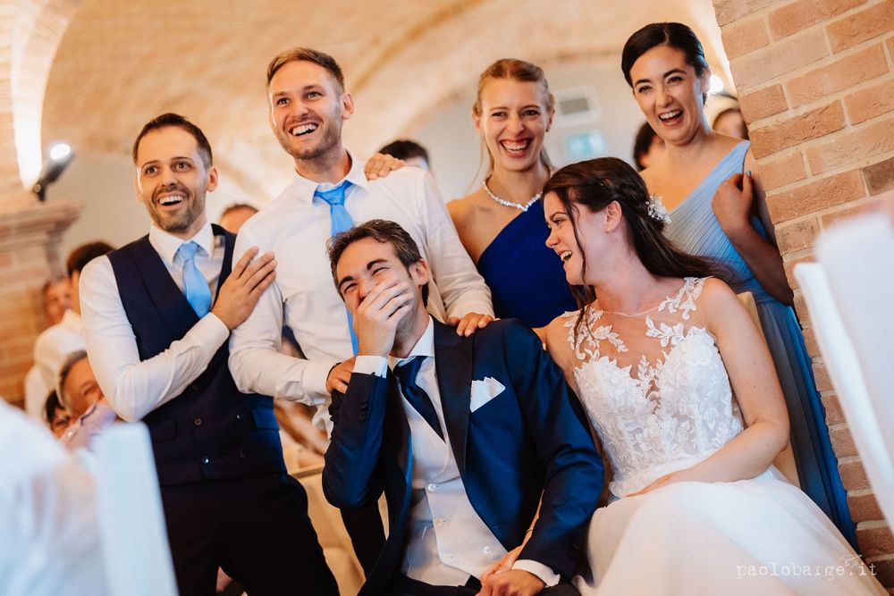Wedding party celebrates joyfully under brick arches at reception venue.
