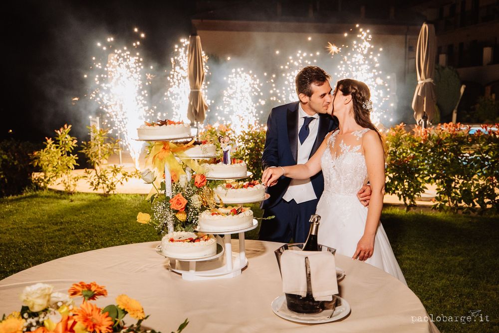 Newlyweds cut their wedding cake with sparklers creating a magical backdrop in the garden.