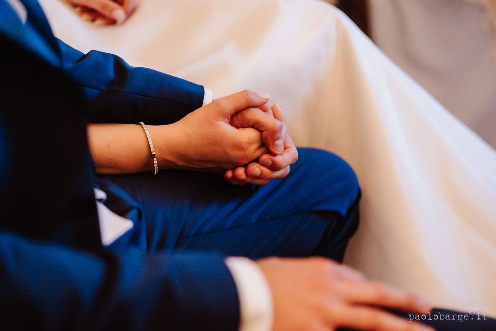 Close-up shot of clasped hands in formal attire during an emotional wedding ceremony moment.