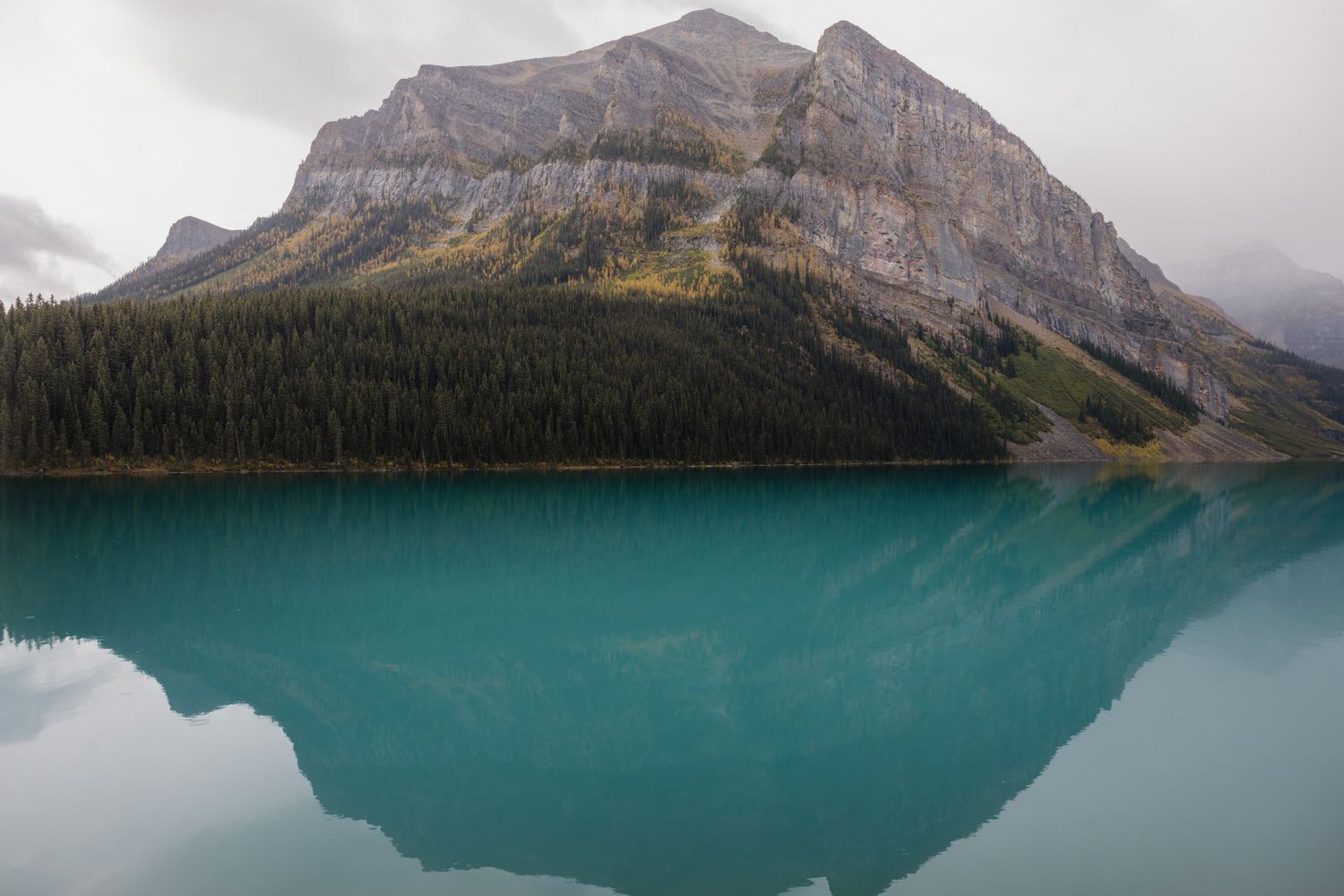 Turquoise glacial lake reflecting a rugged mountain peak surrounded by evergreen forest under overcast skies in Canada. Minot, ND photograph