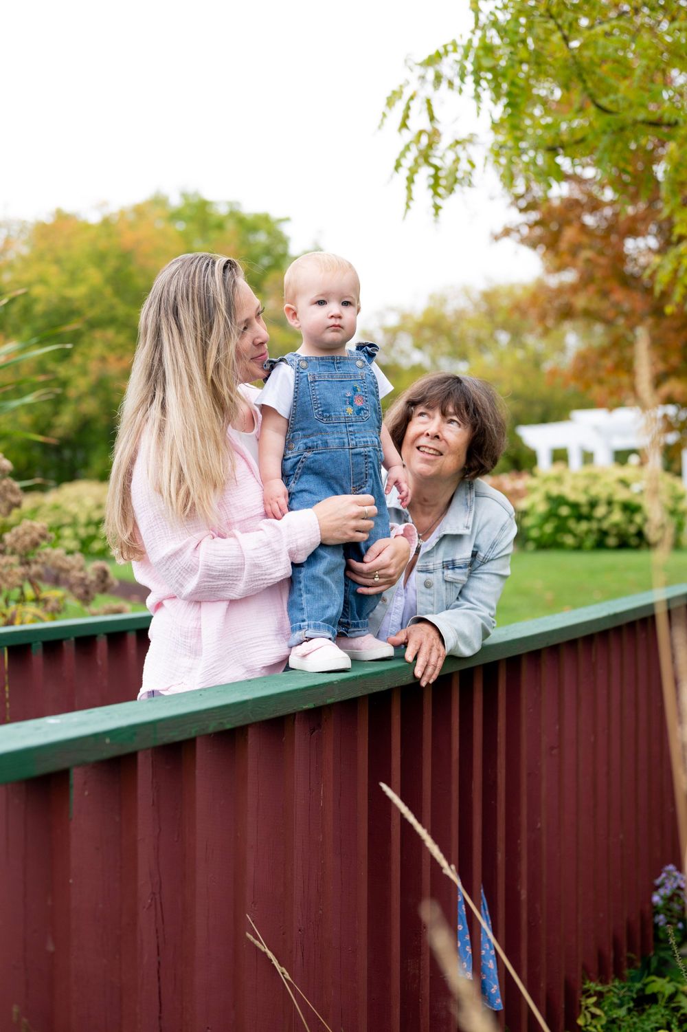 Three generations share a joyful moment together on a red fence in an autumn garden setting.